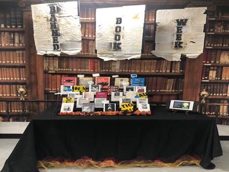Three burned banners that say "Banned Books Week" hang above a display table of banned books