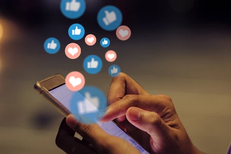 Hands using a smartphone with social media icons floating above.