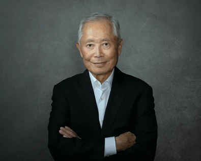 Older man in black jacket and button up shirt on a dark background