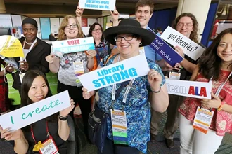 Group of ALA Members smiling and holding library advocacy signs with messages at ALA Annual
