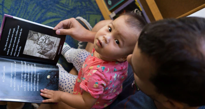 a papa reads with his baby in the library