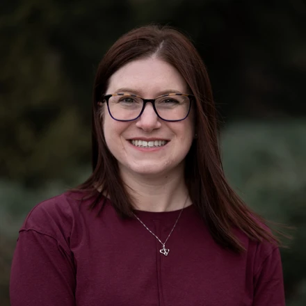 Image of Whitney Kramer, a white woman with brown hair and glasses wearing a maroon dress.